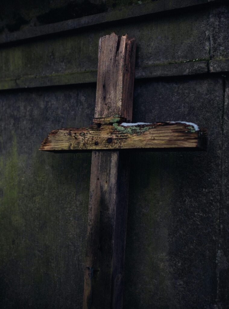 A rustic wooden cross leaning against a concrete wall, symbolizing faith and time.
